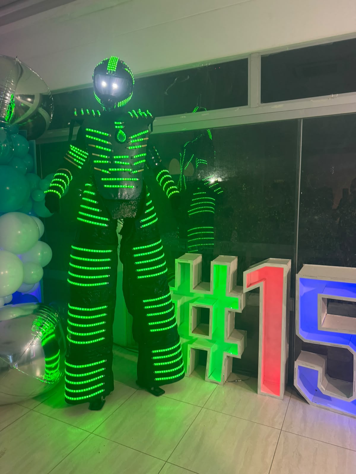 Robô de LED verde em pernas de pau animando festa de 15 anos